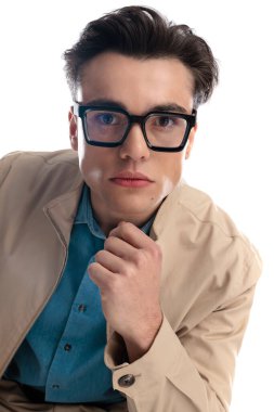 Gözlüklü yakışıklı, dirseği dizinde oturan ve beyaz arka planda ileriye bakan.