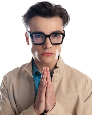 Avuç içlerini bir arada tutan ve beyaz arka planda dua eden yakışıklı genç adamın portresi.