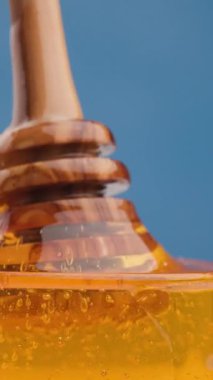 Kaşık kavanoza girerken Holden Bal kıvrılır, Yapışkan, pürüzsüz akışını ve stüdyonun mavi arka planında organik parıltısını gözler önüne serer