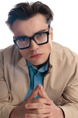 Siyah gözlüklü rahat bir adamın portresi öne bakıyor ve beyaz arka planda otururken el ele tutuşuyor.