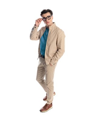Beyaz arka planda el ele yürürken bej ceketli, gözlük takan seksi bir adam.
