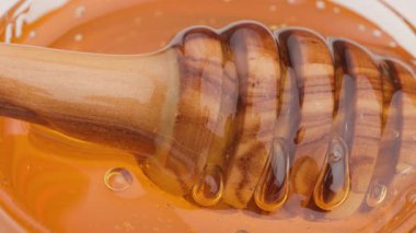 Kavanozda dönen ve pürüzsüz ve doğal organik şurubu gösteren ahşap kaşığın üzerindeki altın tatlı balı yavaş çekim videosu.