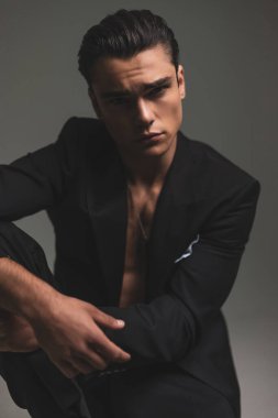 Siyah smokinli çekici bir adamın portresi. Gri arka planda diziyle havalı poz veriyor.