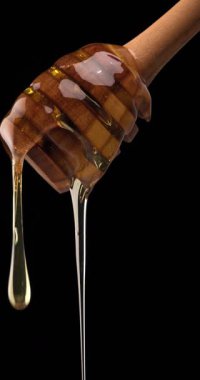 Bal dolu ahşap kaşık siyah arkaplan önünde kalın ve lüks dokusunu gösteriyor.