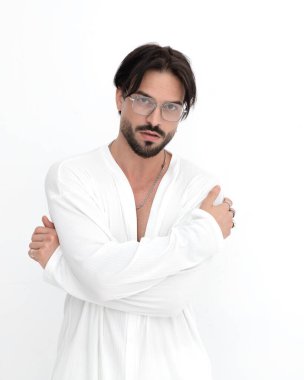 Beyaz arka planda kameraya bakarken kollarını kavuşturan gözlüklü çekici bir gencin portresi.