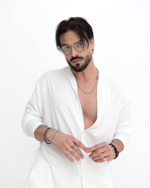 Gözlüklü, beyaz kostümlü, kameraya bakıp beyaz arka planda poz veren havalı bir moda adamı portresi.