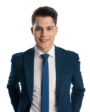 Mutlu, lacivert takım elbiseli, elleri cebinde kravatlı ve beyaz arka planda poz veren zarif bir adam.