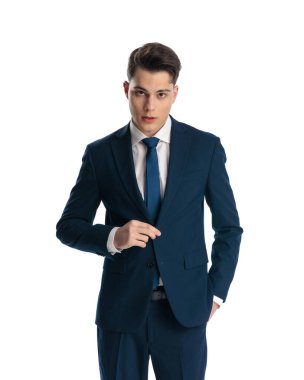 Çekici, zarif bir adam lacivert takımı tamir ediyor ve beyaz arka planda poz verirken cebinde el ele duruyor.