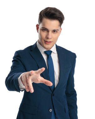 Lacivert takımlı yakışıklı genç adam el hareketi yapıyor ve beyaz arka planda gülümsüyor.