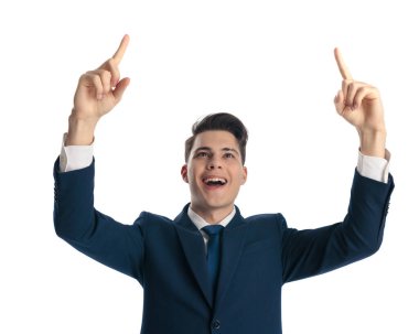 Zarif lacivert takım elbiseli heyecanlı işadamı parmaklarını başının üstünde gösteriyor, gülüyor ve beyaz arka planda gururlanıyor.