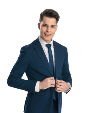 Mutlu zarif bir adamın portresi gülümserken lacivert takımını ilikliyor ve beyaz arkaplan önünde poz veriyor.