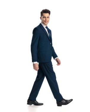 Lacivert takım elbiseli, gülümseyen ve beyaz arka planda yürüyen mutlu genç iş adamının yan görüntüsü.