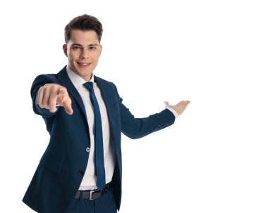 Lacivert takımlı mutlu ve zarif bir adam beyaz arka planda öne doğru işaret ediyor.