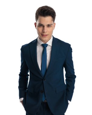 Lacivert takım elbiseli mutlu bir genç. Kravatını cebine sokup beyaz arka planda gülümsüyor.