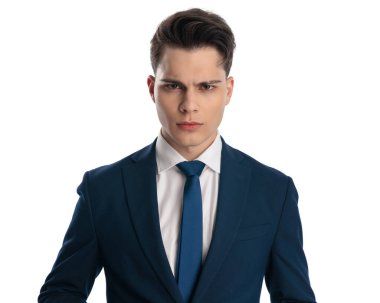 Lacivert takım elbiseli üzgün genç bir işadamı kızgın bir ifade takınıyor ve beyaz arka planda kaşlarını çatıyor.