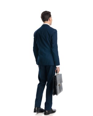 Bavul tutan lacivert takım elbiseli ve beyaz arka planda duran genç işadamlarının arka görüntüsü.