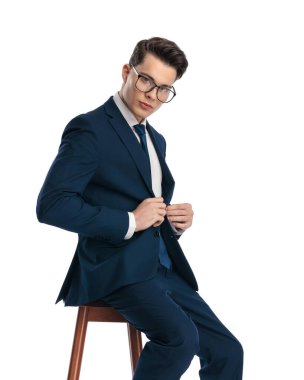 Sınıfı olan kendine güvenen genç bir işadamı lacivert takımı kapatıyor ve beyaz arka planda oturuyor.