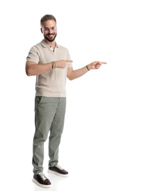 Beyaz arka planda dikilirken gülümseyen ve parmaklarını sağa sola gösteren gözlüklü yakışıklı sıradan bir adam.