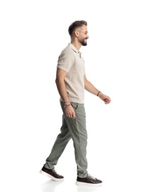 Beyaz arka planda yürürken yan tarafa bakan ve gülümseyen gözlüklü çekici genç adamın yan görünüşü