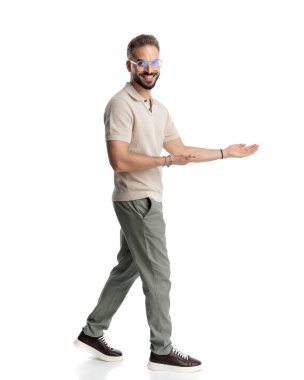 Beyaz arka planda yürürken gülümseyen ve davetli gözlüklü gururlu genç adam.