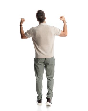 Genç bir adamın yumruklarını havada tutması ve zaferi beyaz arka planda yürürken kutlaması.