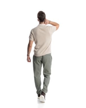 Boynunu tırmalayan ve beyaz arka planda yürüyen seksi genç adam manzarasının arkasında.