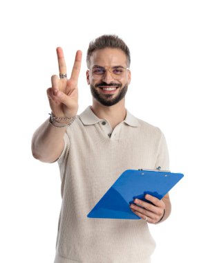 İki parmağını gösteren ve beyaz arka planda gülümseyen mutlu genç bir adam.