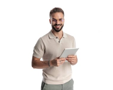 Beyaz arka planda tableti tutarken gülümseyen gözlüklü çekici bir adamın portresi.