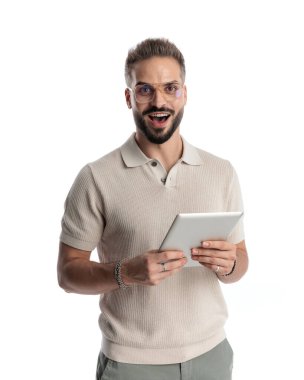 Tablet tutan etkileyici genç adam, şaşırdı ve beyaz arkaplan önünde ağız açıyor