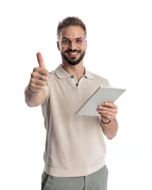 Gözlüklü mutlu adam beyaz arka planda gülümserken başparmak hareketi yapıyor ve tableti tutuyor.