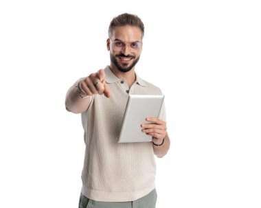 Gözlüklü, tablet tutan ve beyaz arkaplan önünde parmağını öne doğru gösteren yakışıklı sıradan bir adamın portresi.