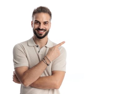 Polo tişörtlü mutlu bir adamın portresi gülümseyen ve beyaz arka planda kollarını kavuştururken parmaklarını sağa sola gösteren.