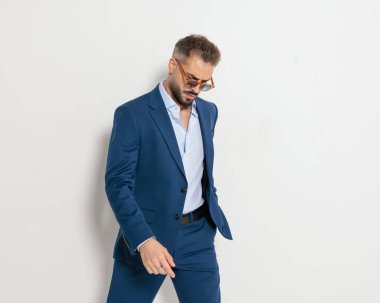 Güneş gözlüklü genç ve seksi iş adamı gri arka planda el ele poz veriyor.