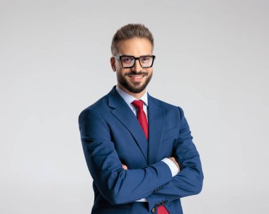 Lacivert takımlı mutlu zarif adam kollarını kavuşturup beyaz arka planda gülümsüyor.