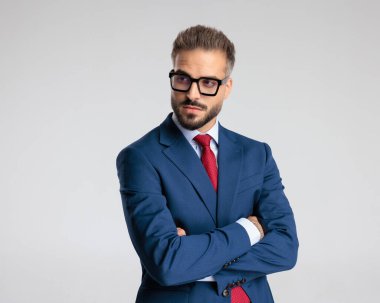 Gözlüklü seksi sakallı iş adamı. Gri arka plan önünde kırmızı kravatlı lacivert bir takım elbise giyiyor.