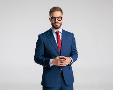 Lacivert takım elbiseli zarif bir gencin portresi. El ele tutuşup gri arka planda poz veriyor.