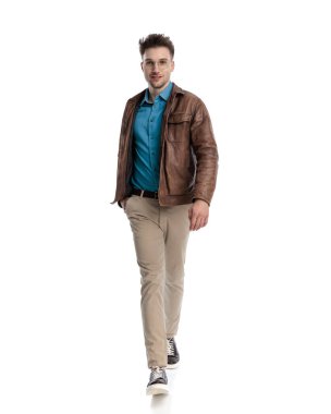 Gözlüklü mutlu genç adam bahar ceketi giyiyor, gülümsüyor ve beyaz arka planda yürüyor.