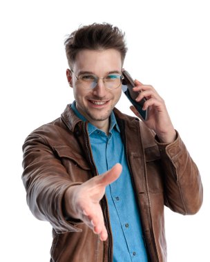 Kahverengi deri ceketli, gözlüklü, telefonla konuşan, el ele tutuşan beyaz arka planda selamlaşan ve gülümseyen kibar bir adam.