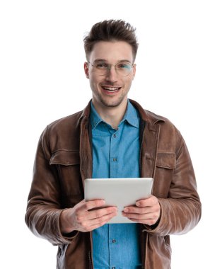 Kahverengi deri ceketli, tablet tutan ve beyaz arka planda gülümseyen sarışın sıradan bir adamın portresi.