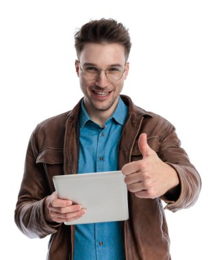 Tablet tutan, gülümseyen ve beyaz arkaplan önünde baş parmak hareketi yapan gururlu sıradan bir adam.