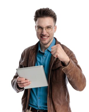 Kahverengi deri ceketli, beyaz arka planda tablet tutarken zaferi kutlayan hevesli sıradan bir adam.