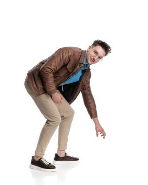 Kahverengi deri ceketli yakışıklı genç adam beyaz arka planda yerden bir şey alıyor.