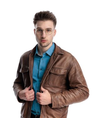 Gözlüklü çekici sarışın adam beyaz arka planda kahverengi deri ceketi tamir ediyor.