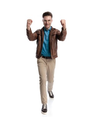 Beyaz arka planda yürürken yumruklarını kaldırıp zaferi kutlayan gururlu genç adamın tüm vücudu.