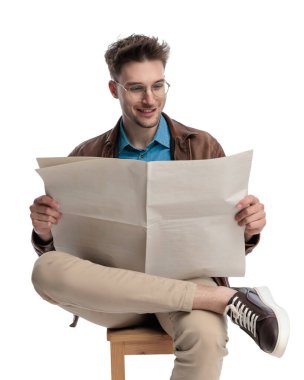 Gözlüklü, gülümseyen ve gazete okuyan mutlu bir adam beyaz arka planda dizlerinin üstüne çöküp oturuyor.