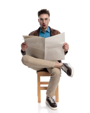 Gözlüklü genç adam gazete okuyor ve beyaz arka plandaki haberler karşısında şok oluyor.