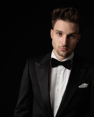 Siyah smokinli yakışıklı genç damat. Siyah arka plan önünde papyonlu.