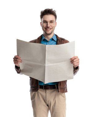 Gözlüklü mutlu genç adam gazete okuyor ve beyaz arka planda gülümsüyor.