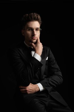 Düşünceli, zarif bir adam siyah arka planda otururken çenesine dokunup düşünüyor.