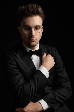 Çekici, gözlüklü, kollarını kavuşturup siyah arka plana bakan zarif bir damat.